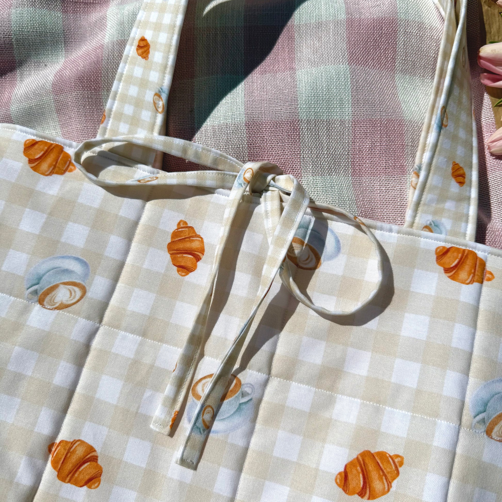 Close-up of a fabric bag with checkered pattern and croissant and coffee design.