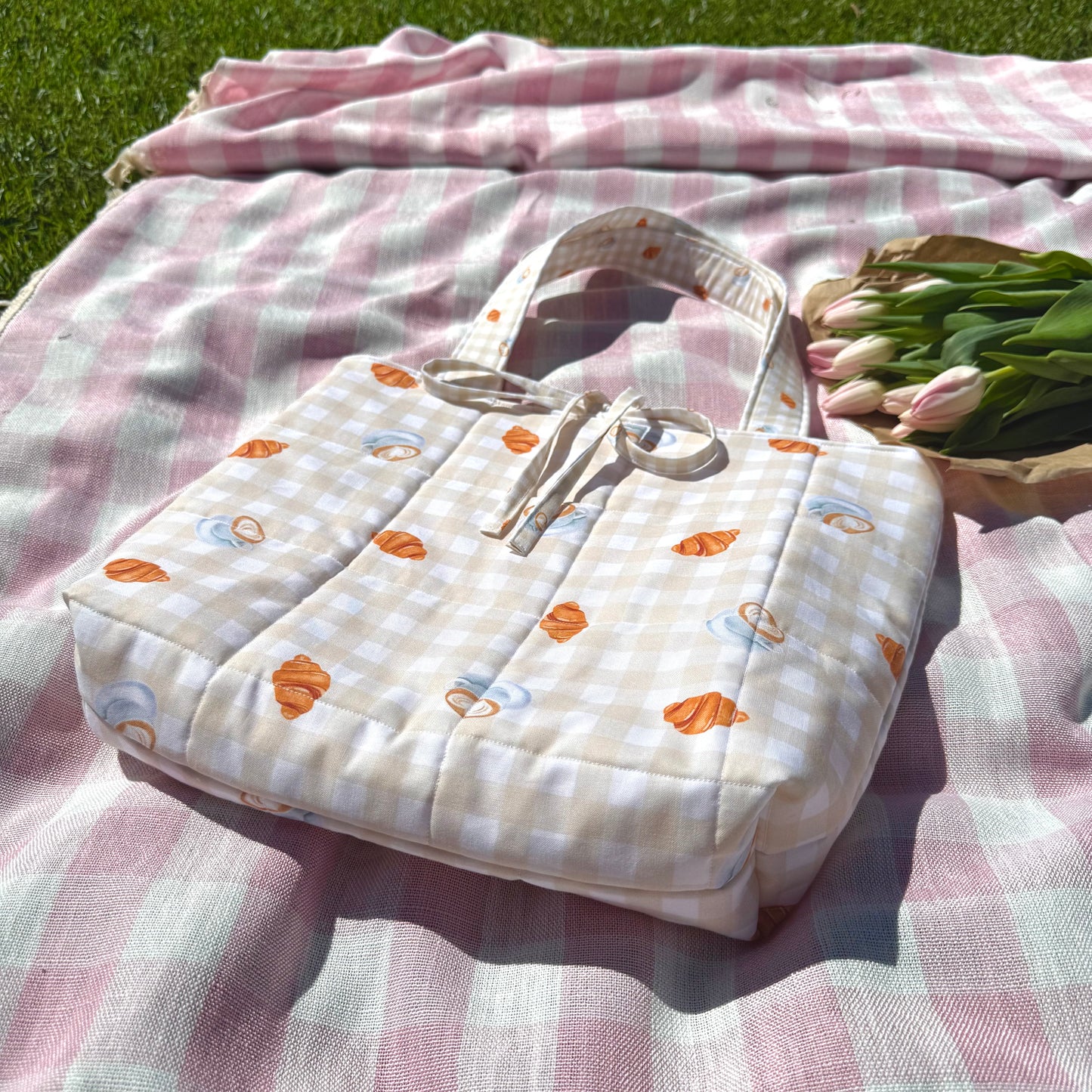 Patterned bag with flowers on a pink checkered blanket outdoors
