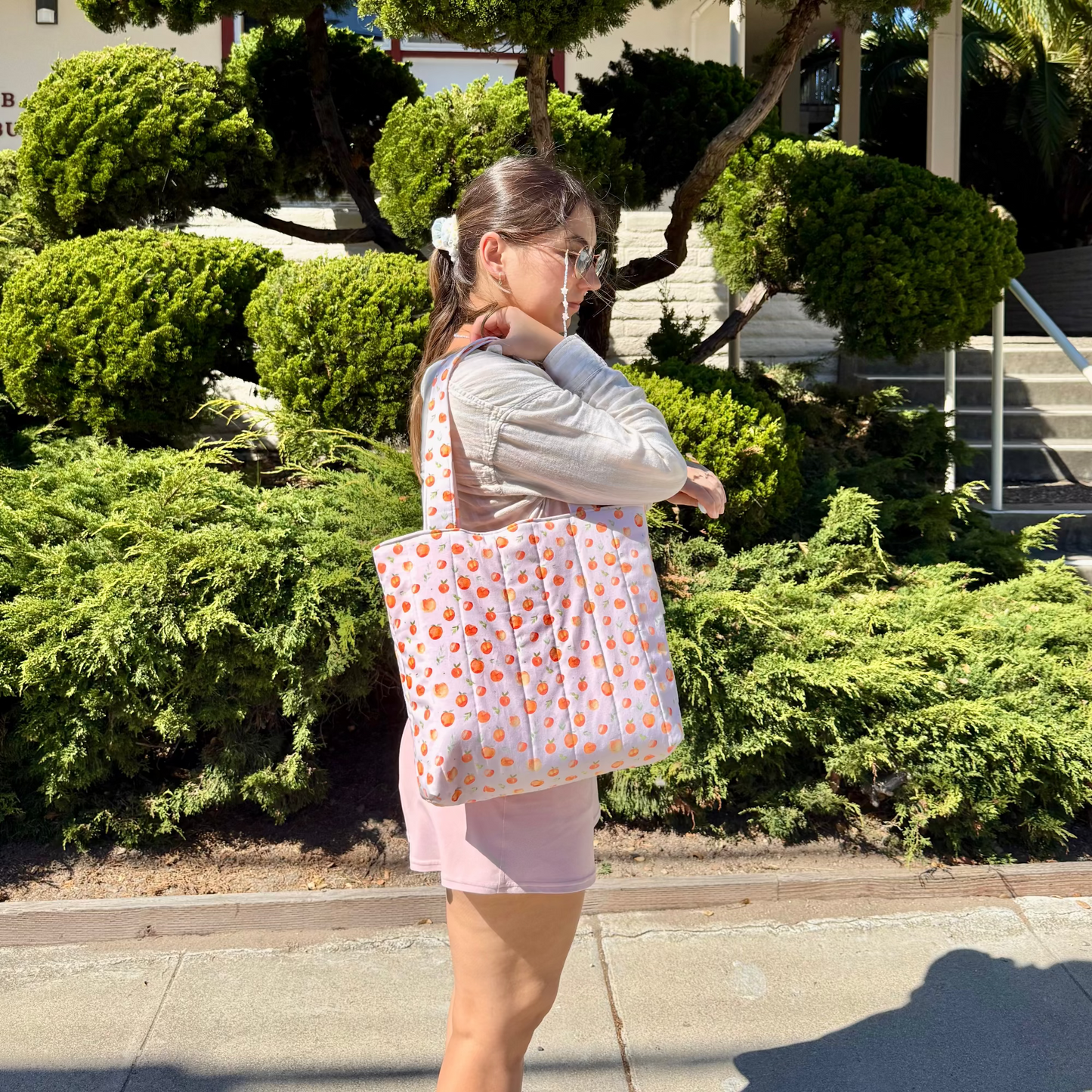 Woman holding a peach patterned bag outdoors with greenery in the background