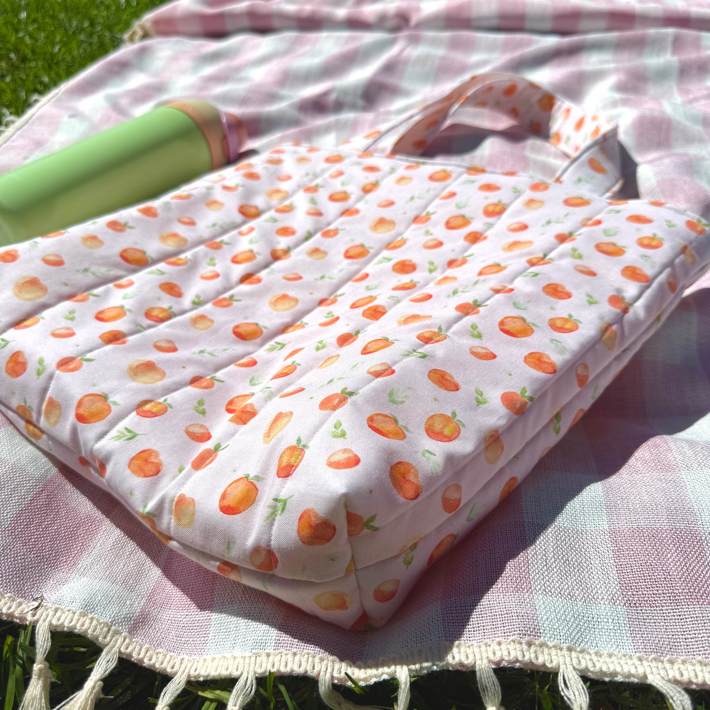 Quilted tote bag with peach fruit pattern on a checkered blanket outdoors