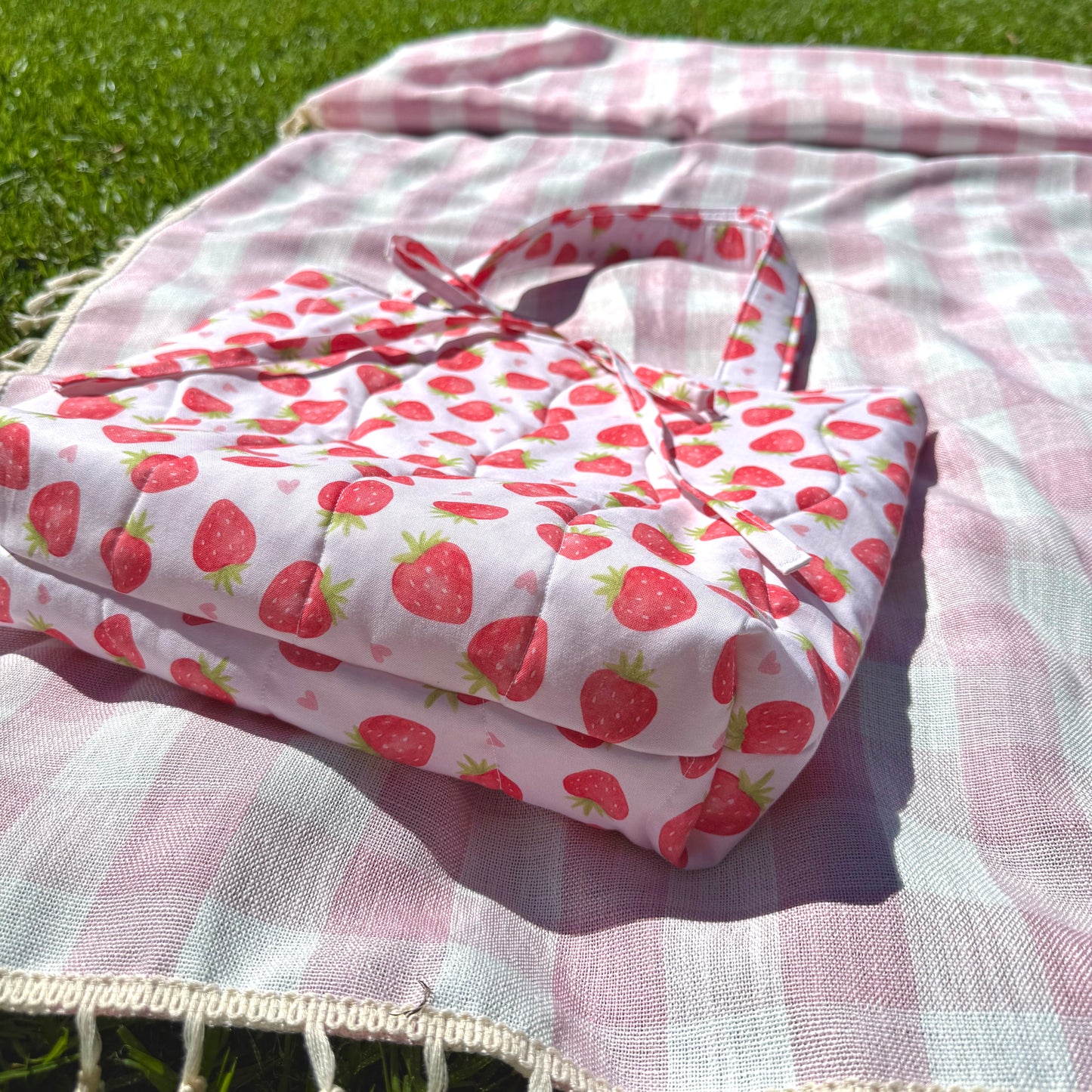 Handmade Strawberry Love tote bag by From Aly photographed on green grass, showing quilted stitching, soft handles, and unique fabric design